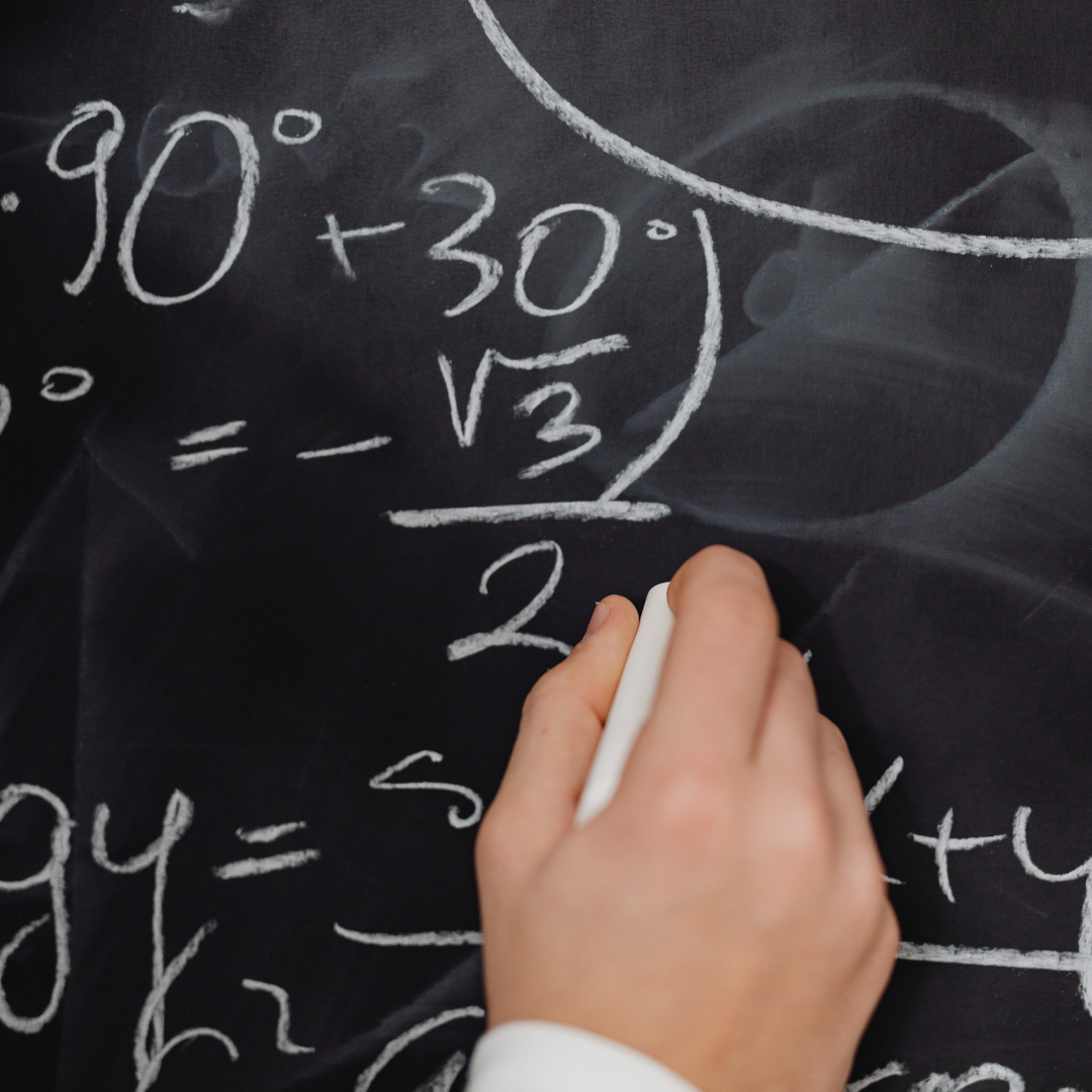 Eine Person schreibt mathematische Gleichungen an eine Tafel. Die Gleichungen enthalten Winkel und Wurzeln, wie beispielsweise „90°, 30° und √3“. Die Hand der Person hält ein Stück weiße Kreide.